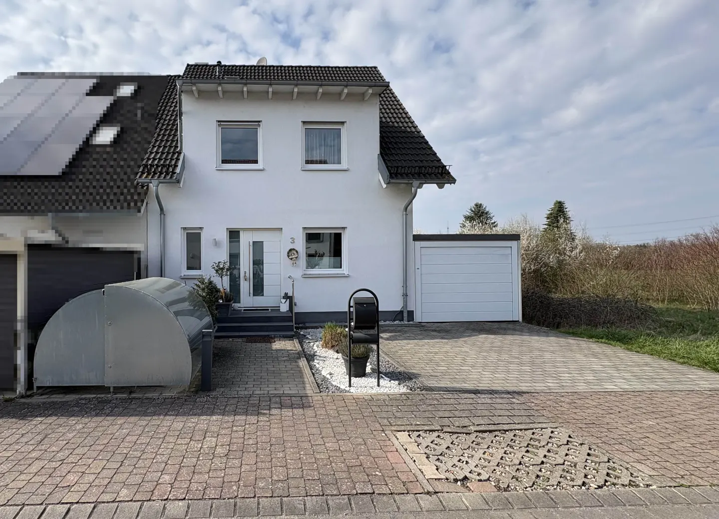 Two-story white house with a dark roof, solar panels, and a white garage. A paved driveway leads to the house.
