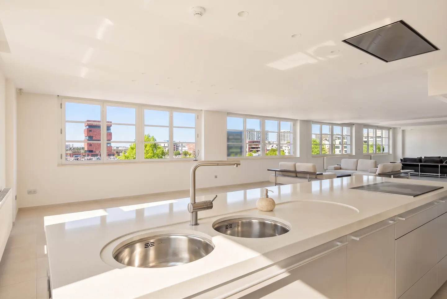 Bright, modern kitchen with white cabinets, stainless steel sink, and large windows overlooking a city.