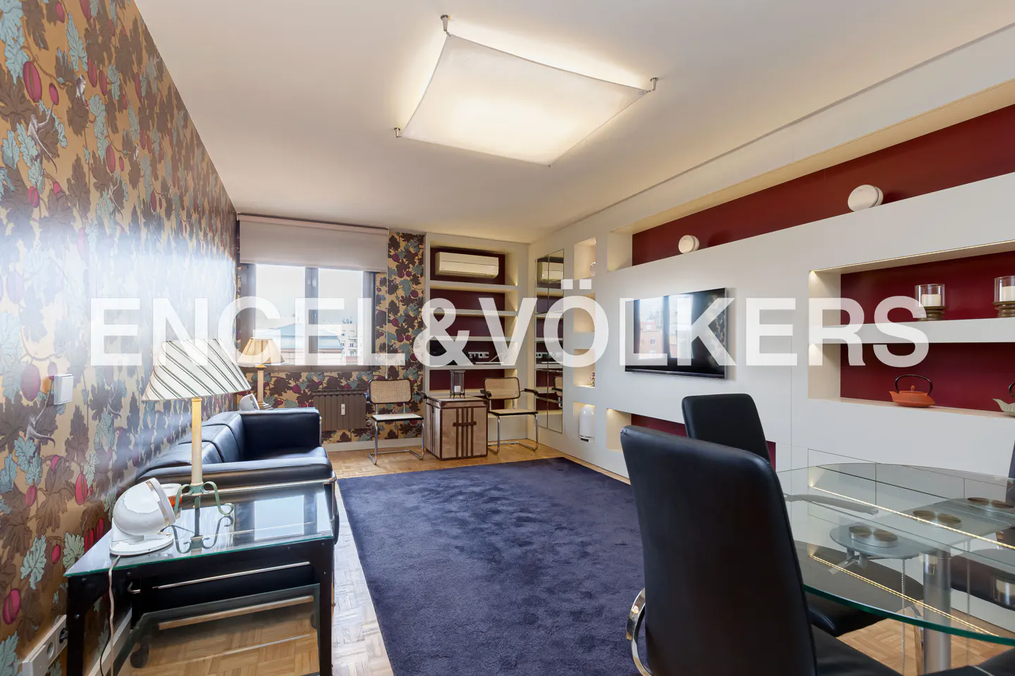 Modern living room with floral wallpaper, a dark blue rug, black leather chairs, and a glass dining table.