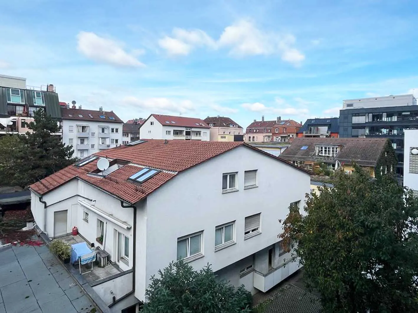 View of a white building with a red tile roof, skylights, and a balcony with furniture, set against a blue sky with clouds.