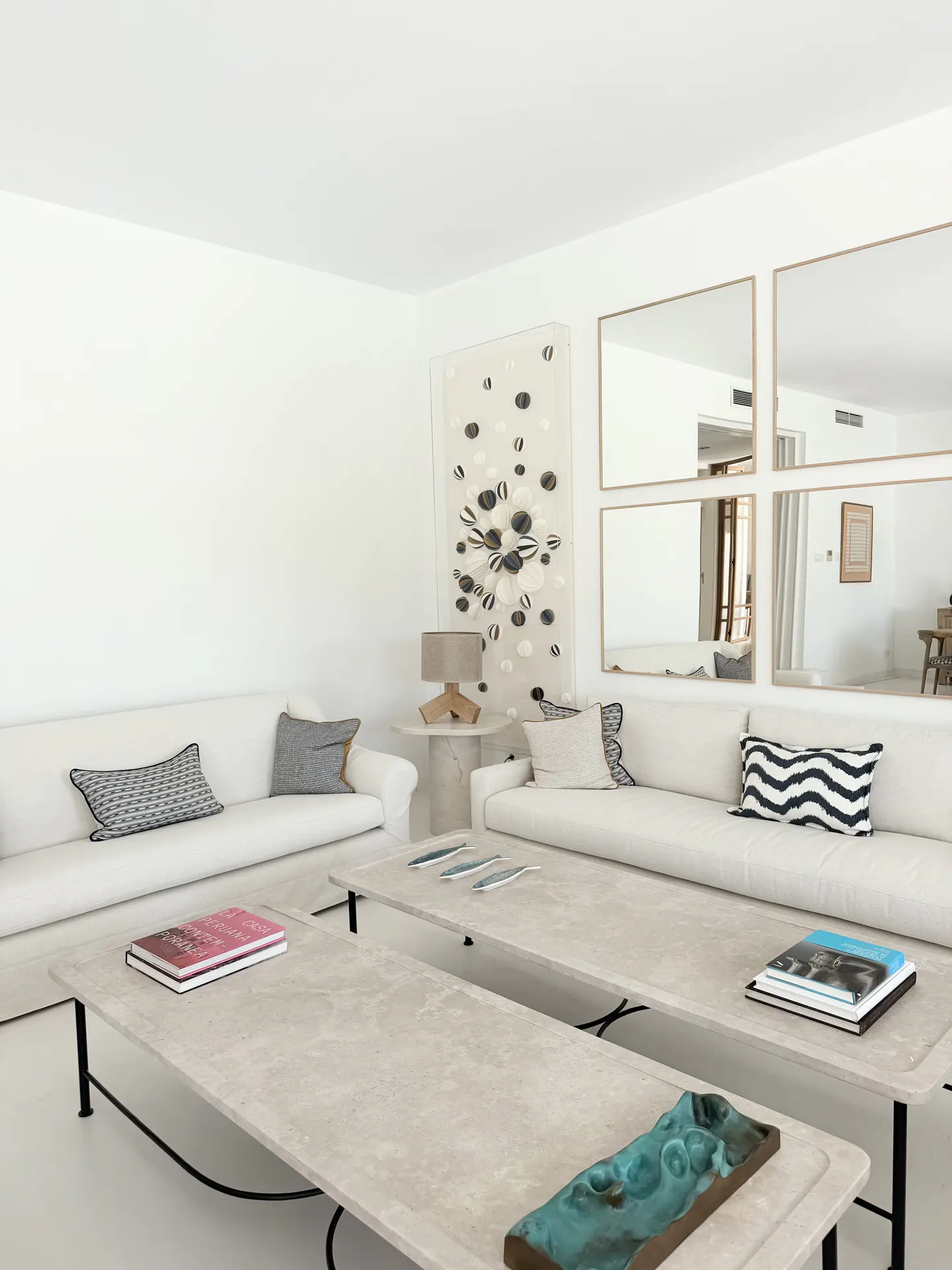 Bright, all-white living room with two sofas, two stone coffee tables, and four square mirrors on the wall.