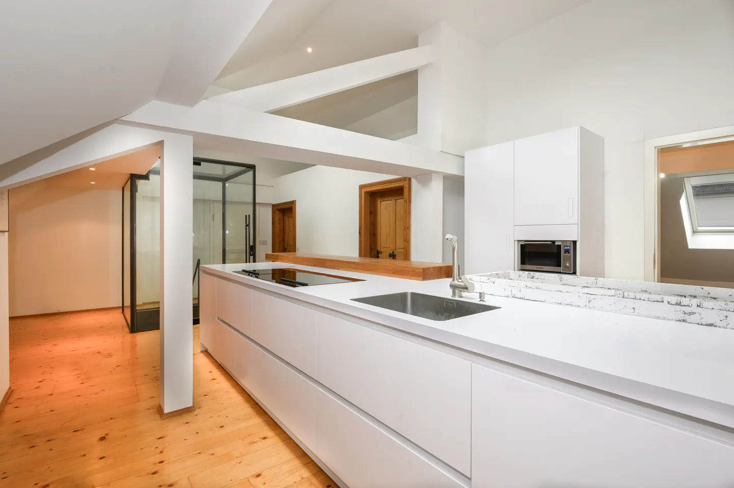 Bright, modern kitchen with white cabinets, countertops, and wood floors. A black-framed glass shower is visible in the background.