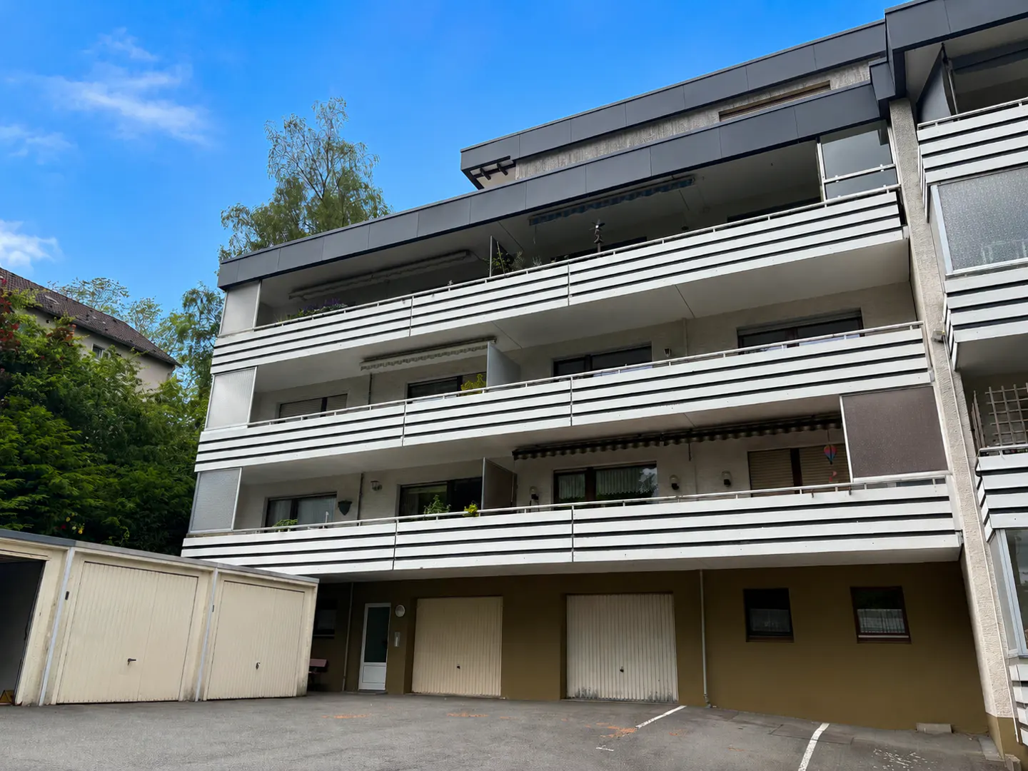 Low-angle view of a modern apartment building with three levels of white balconies and ground-floor garage doors.