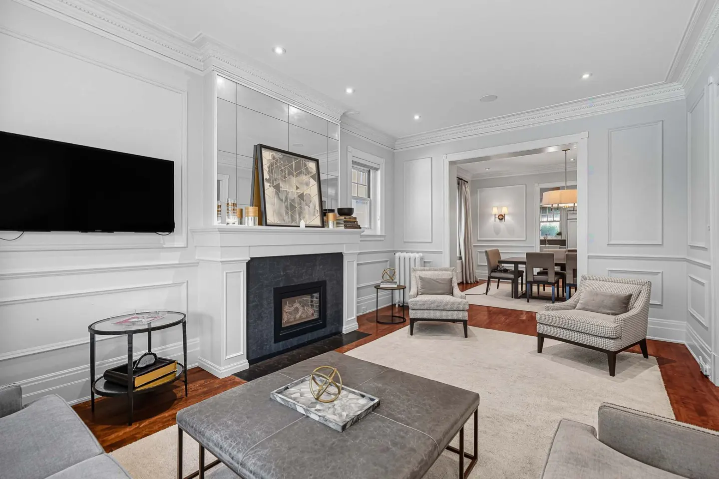 Living room with white walls, fireplace, TV, and gray furniture. Dining room visible in the background.