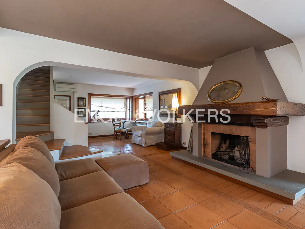 Living room with brown sofa, fireplace, and stairs. The room has terracotta tile flooring and a brown ceiling.