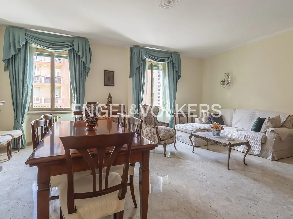 A bright living and dining area with a wooden table, sofa, and blue curtains.
