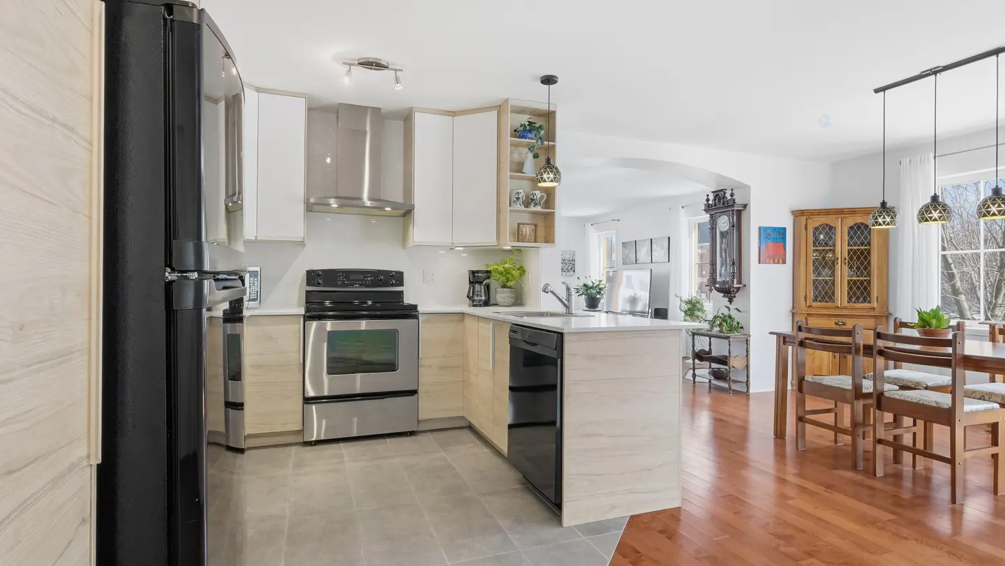 A bright, modern kitchen with stainless steel appliances, white and light wood cabinets, and an open floor plan leading to a dining area.