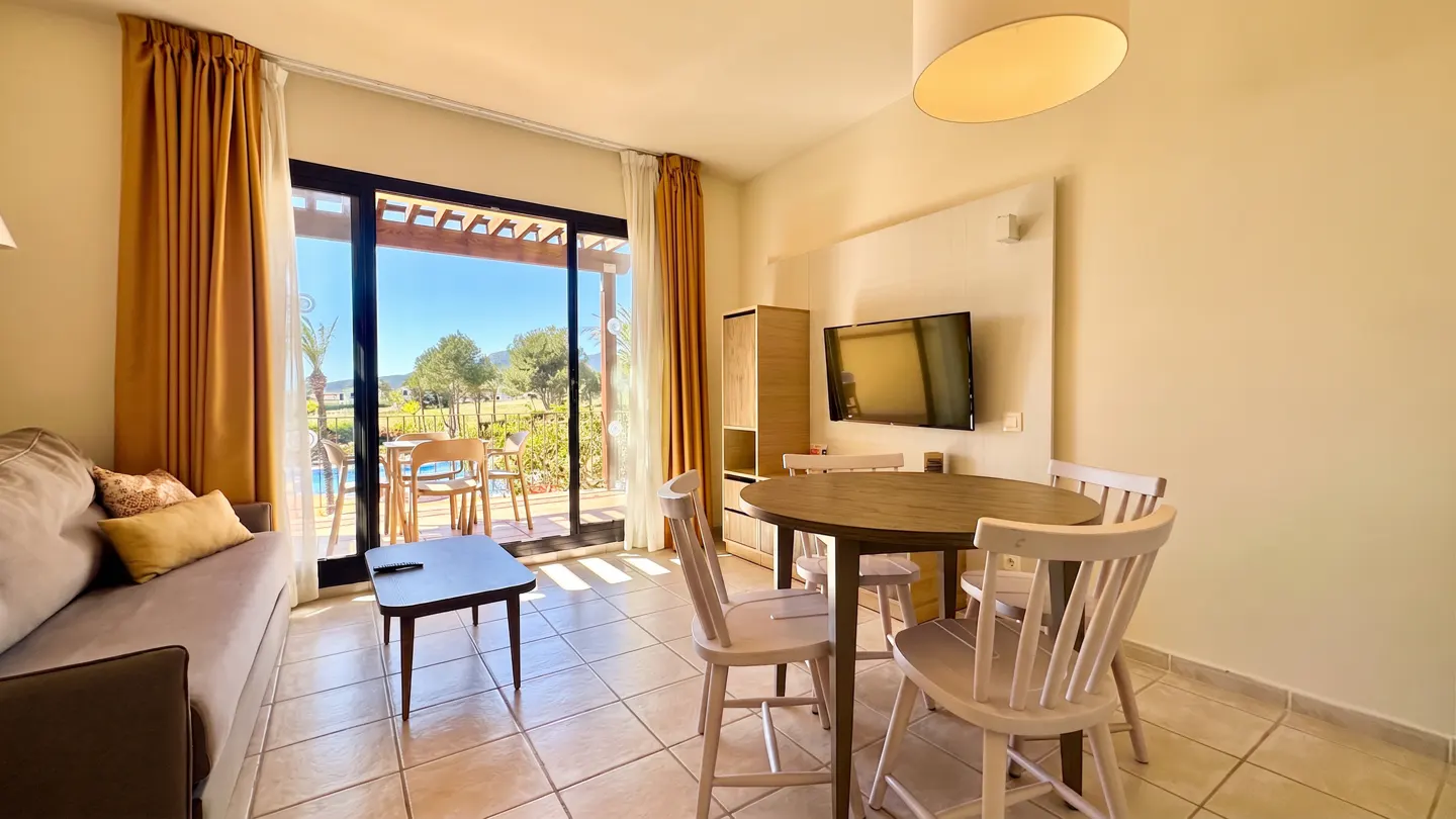 Living room with a brown sofa, round table with four chairs, and a sliding glass door to a patio with a pool view.