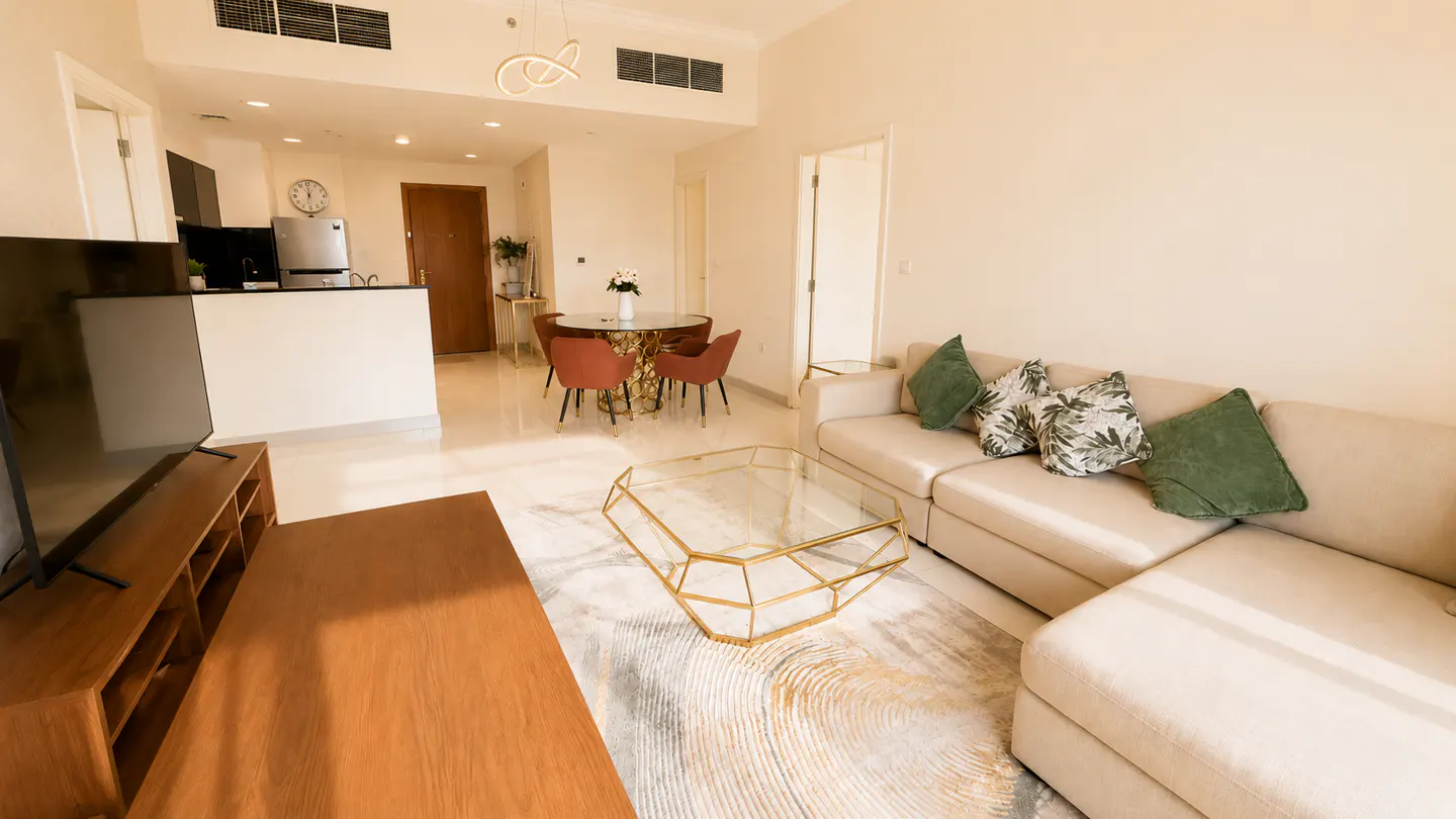 A bright, open-plan apartment with a cream sofa, gold coffee table, and dining area with orange chairs.