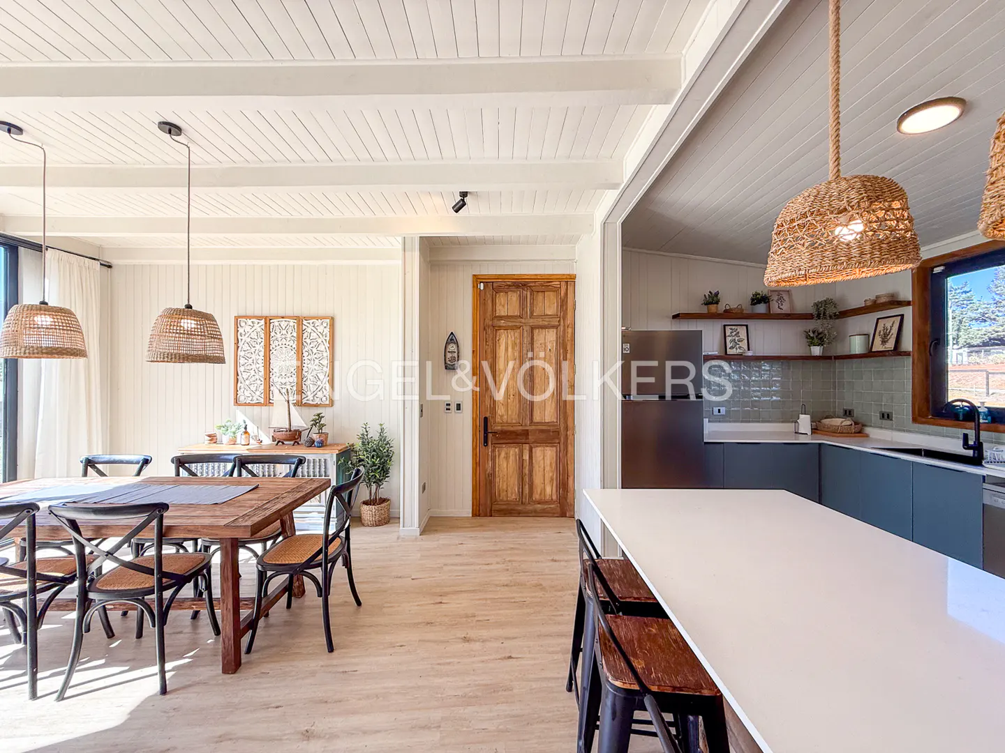 Open-concept dining and kitchen area with wood floors, white walls, and woven pendant lights. Dining table with black chairs.