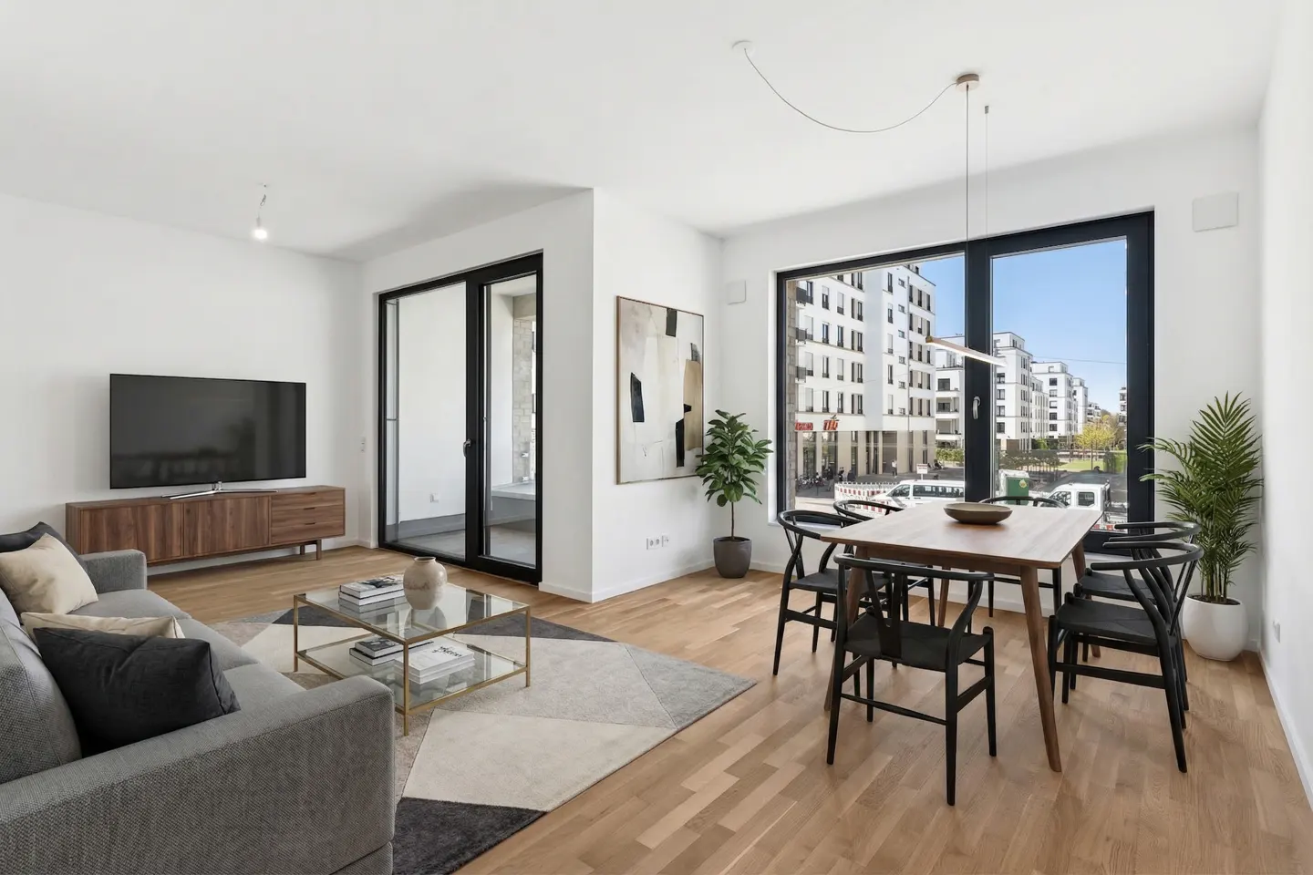 Bright living room with gray sofa, wood table, black chairs, and a large window overlooking a city street.