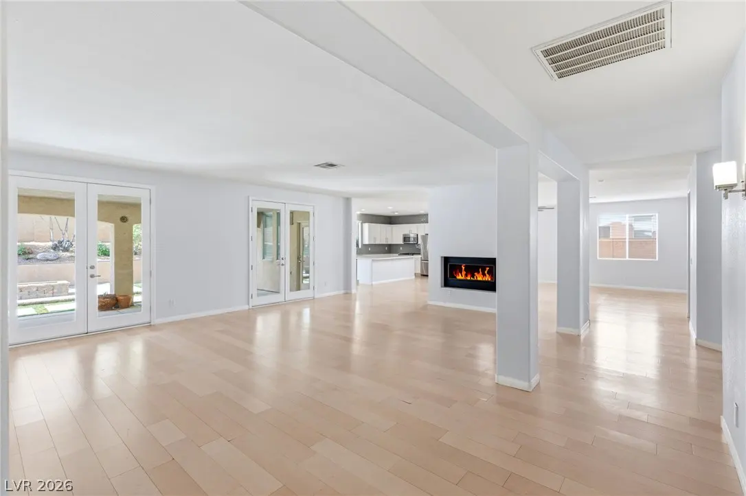 Open-concept living area with light wood floors, a modern fireplace, and glass doors leading to a patio.