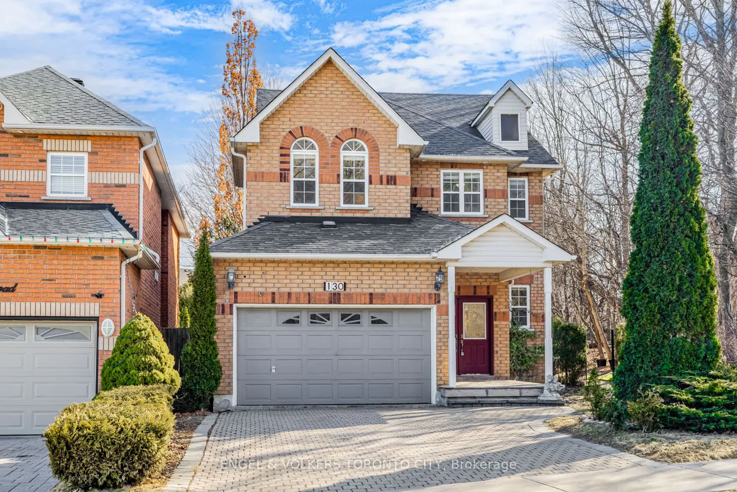Two-story brick house with a gray garage door, red front door, and a well-manicured lawn.