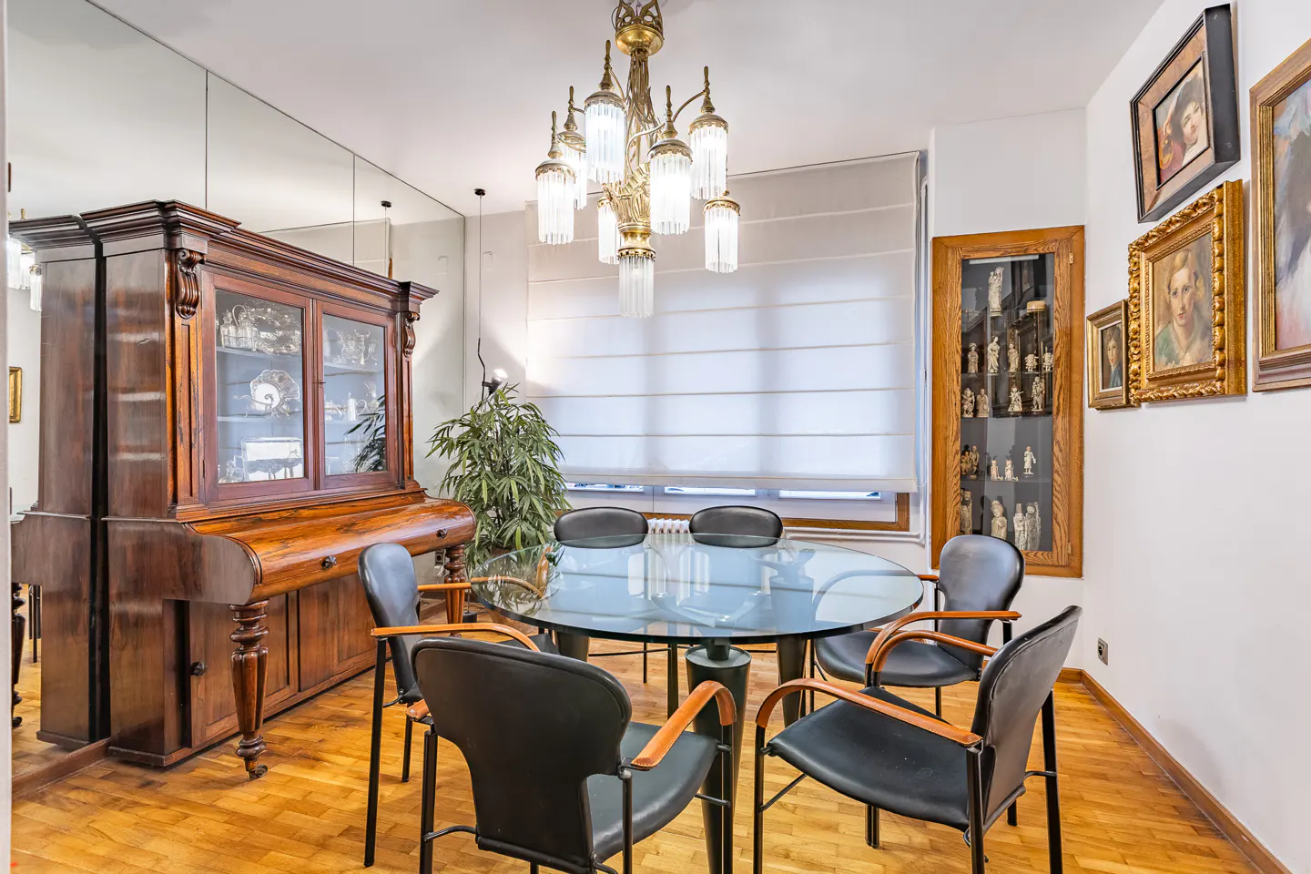 A dining room with a glass table, black chairs, a wooden cabinet, and a chandelier.