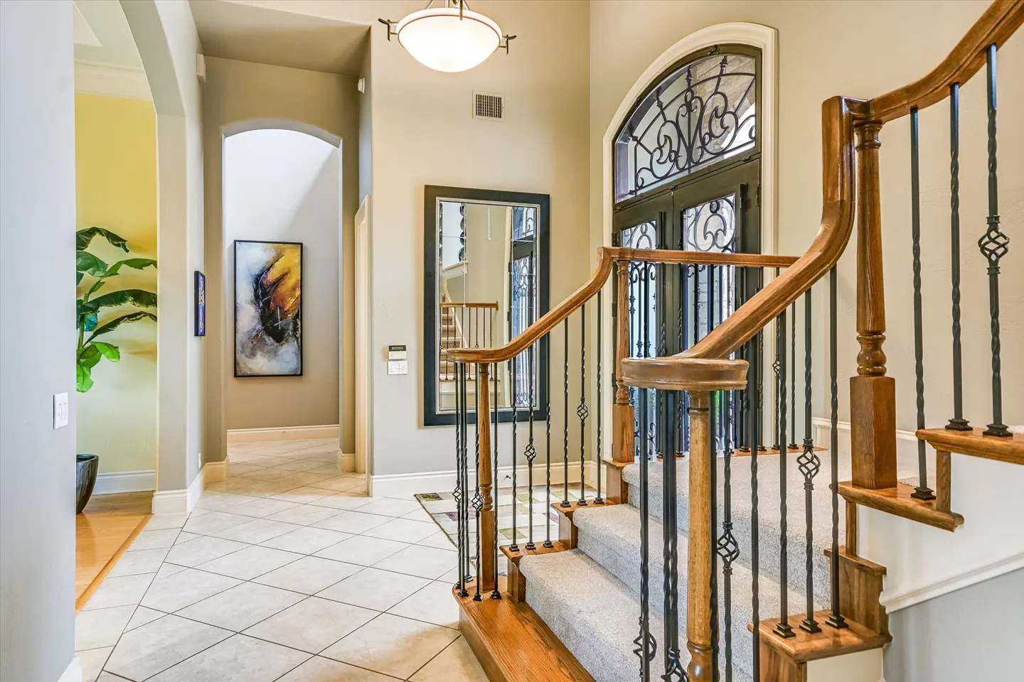 Foyer with staircase, arched doorway, and tiled floor. Wood and iron railing, light fixture, and artwork are visible.