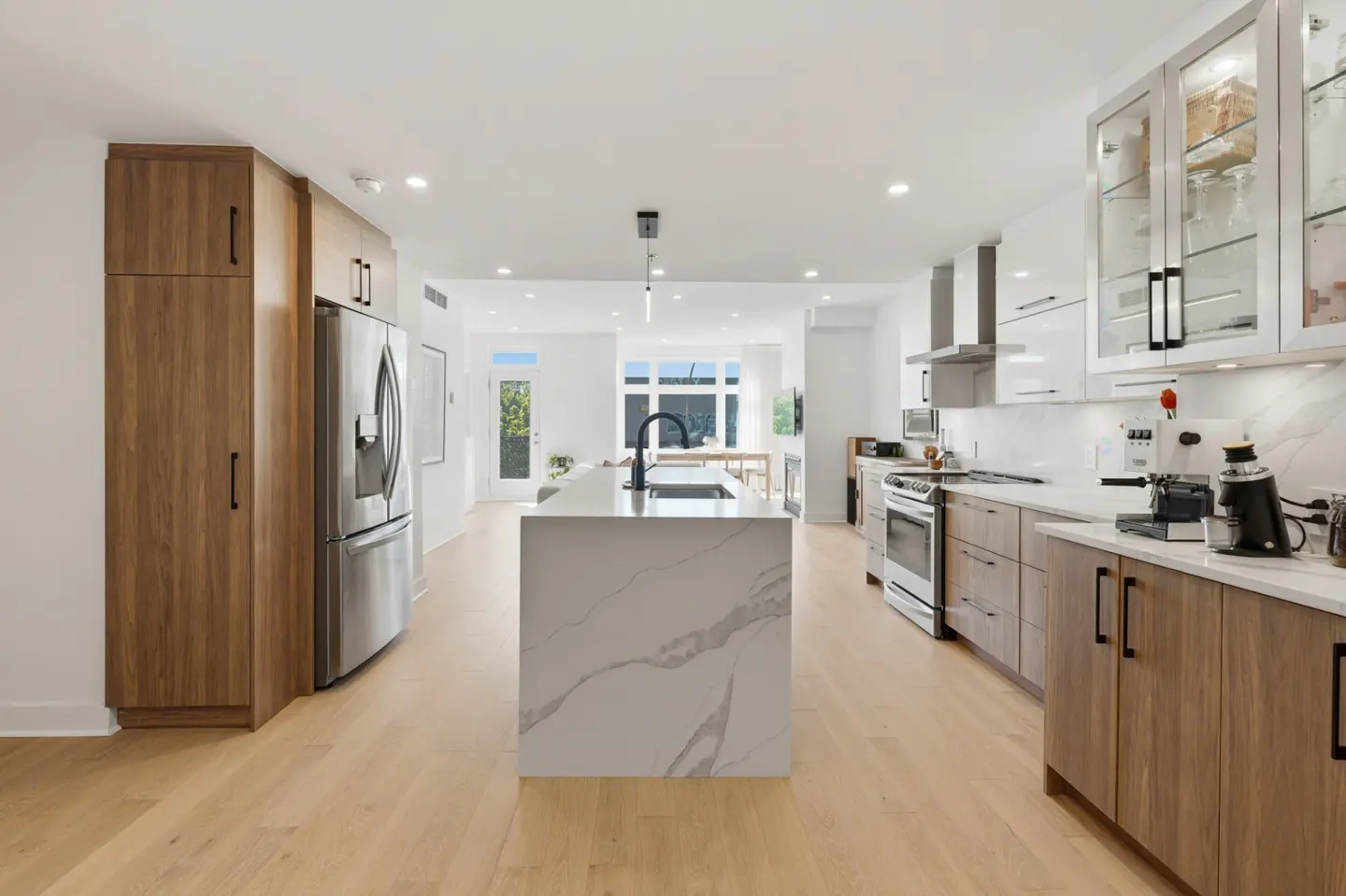 Modern kitchen with wood cabinets, white marble island, stainless steel appliances, and light hardwood floors.