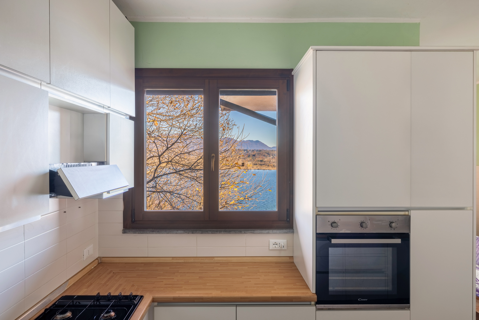 Bright kitchen with white cabinets, wood countertop, and a window view of a lake and autumn trees.