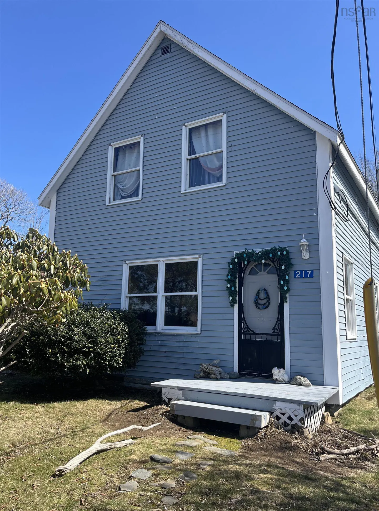 Two-story light blue house with white trim, a decorated front door, and a small porch.