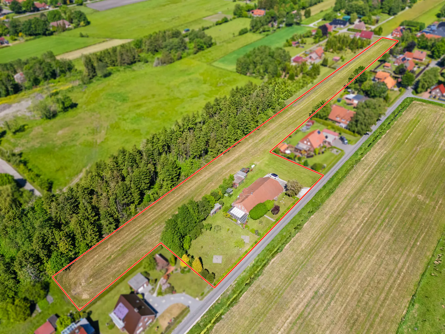 Aerial view of a rural property outlined in red, featuring a house, large lawn, and adjacent forest bordering open fields.