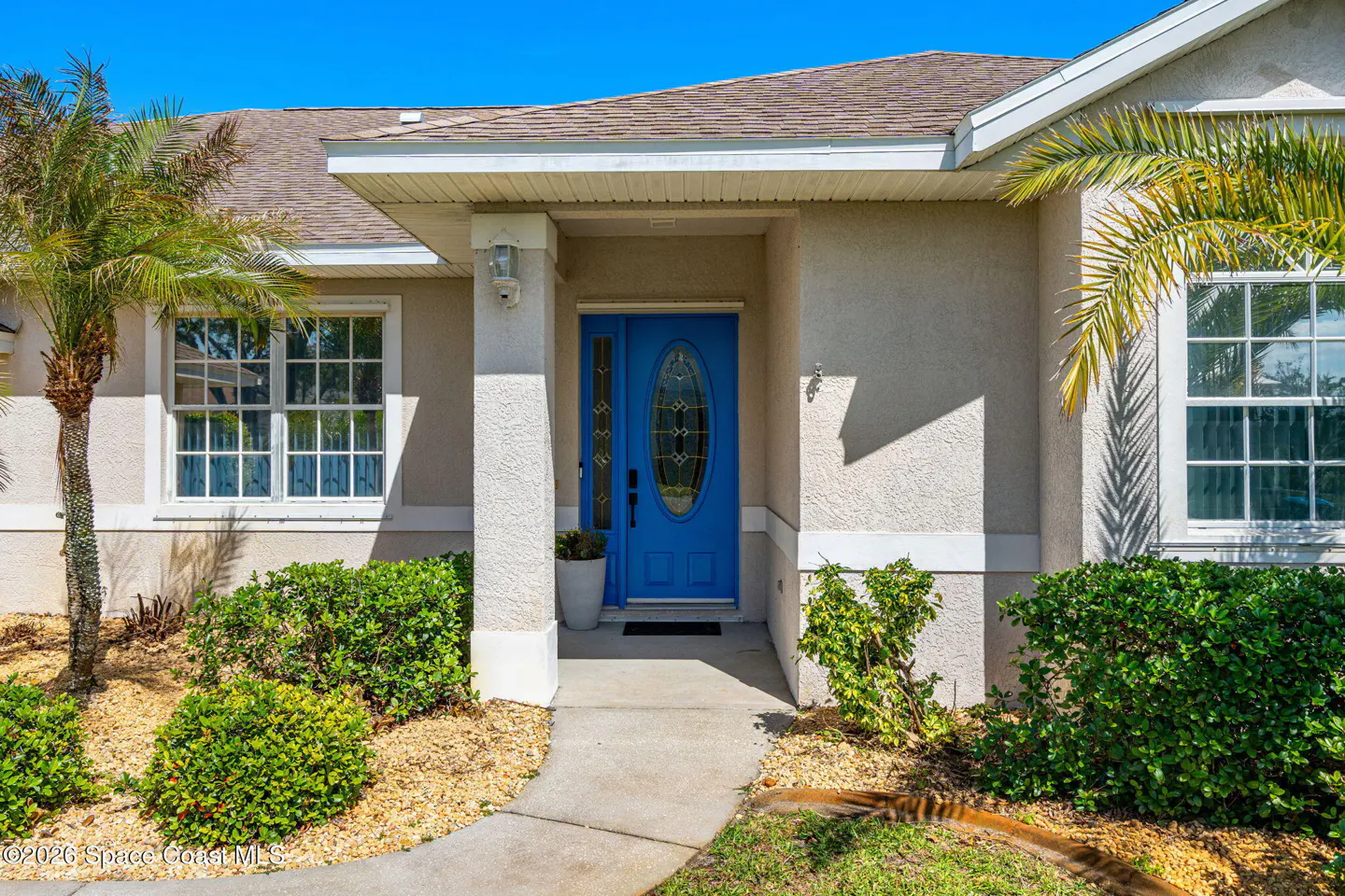 Front exterior of a beige house with a bright blue front door, white trim, and green landscaping.