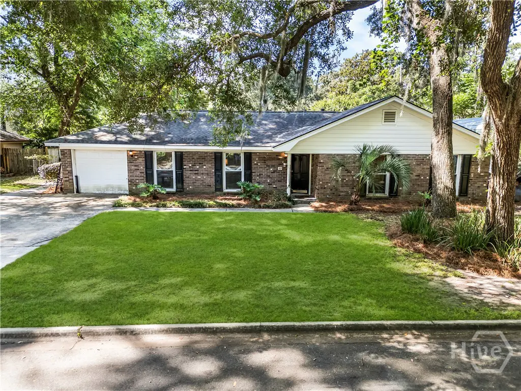 Single-story brick ranch home with white siding, a two-car garage, and a large front lawn under mature oak trees.
