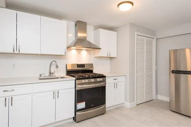 Bright kitchen with white cabinets, stainless steel appliances, and light gray walls. A stainless steel refrigerator is on the right.