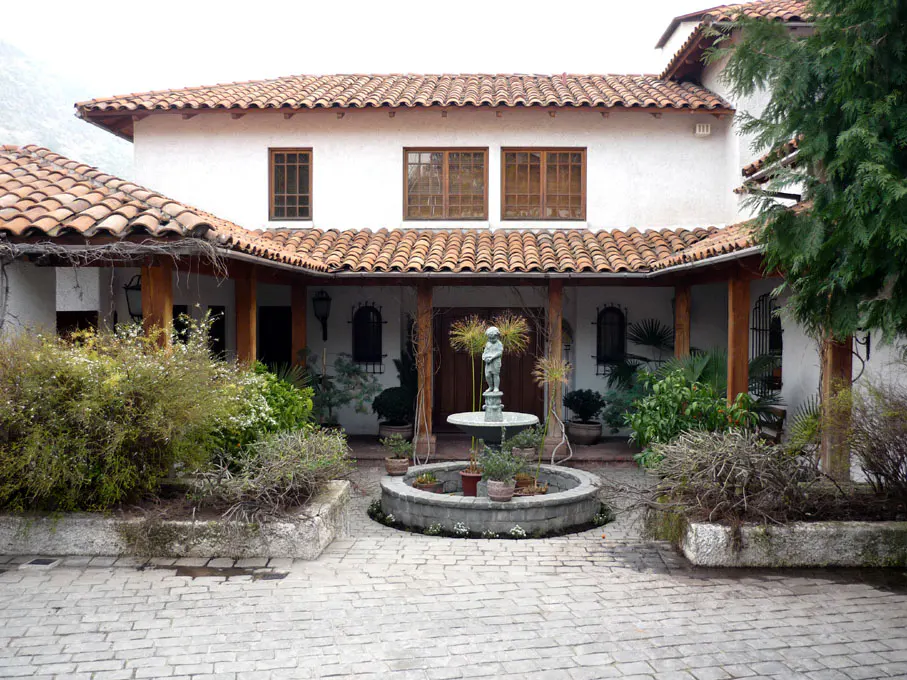 Courtyard view of a white stucco house with a red tile roof and a central fountain.