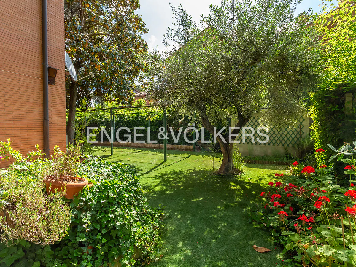Lush green backyard with grass, trees, and red flowers. The Engel & Völkers logo is superimposed on the image.
