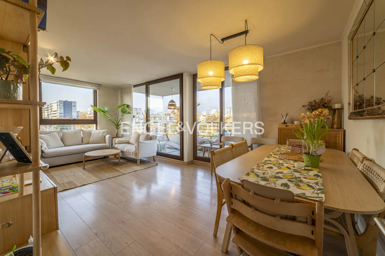 Bright living and dining area with wood floors, sofa, table, and city view through large windows.