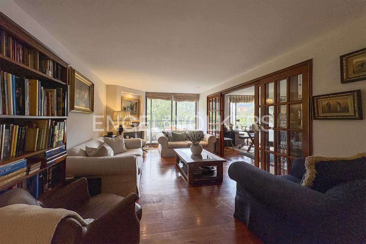A living room with hardwood floors, sofas, a bookshelf, and a view of the outside.