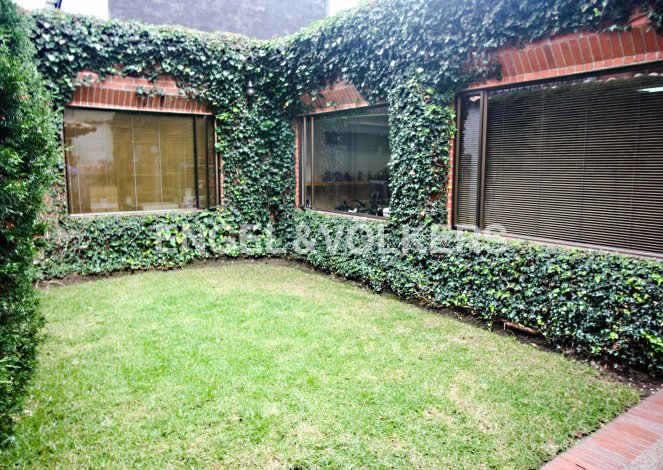A small green lawn is surrounded by a brick building covered in ivy, with windows.