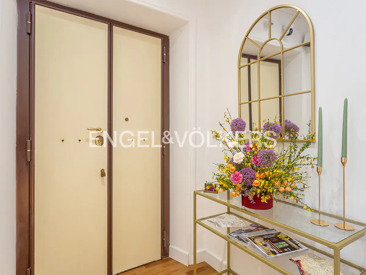 Entryway with a beige door, a gold-framed mirror, and a gold console table with flowers and candles.