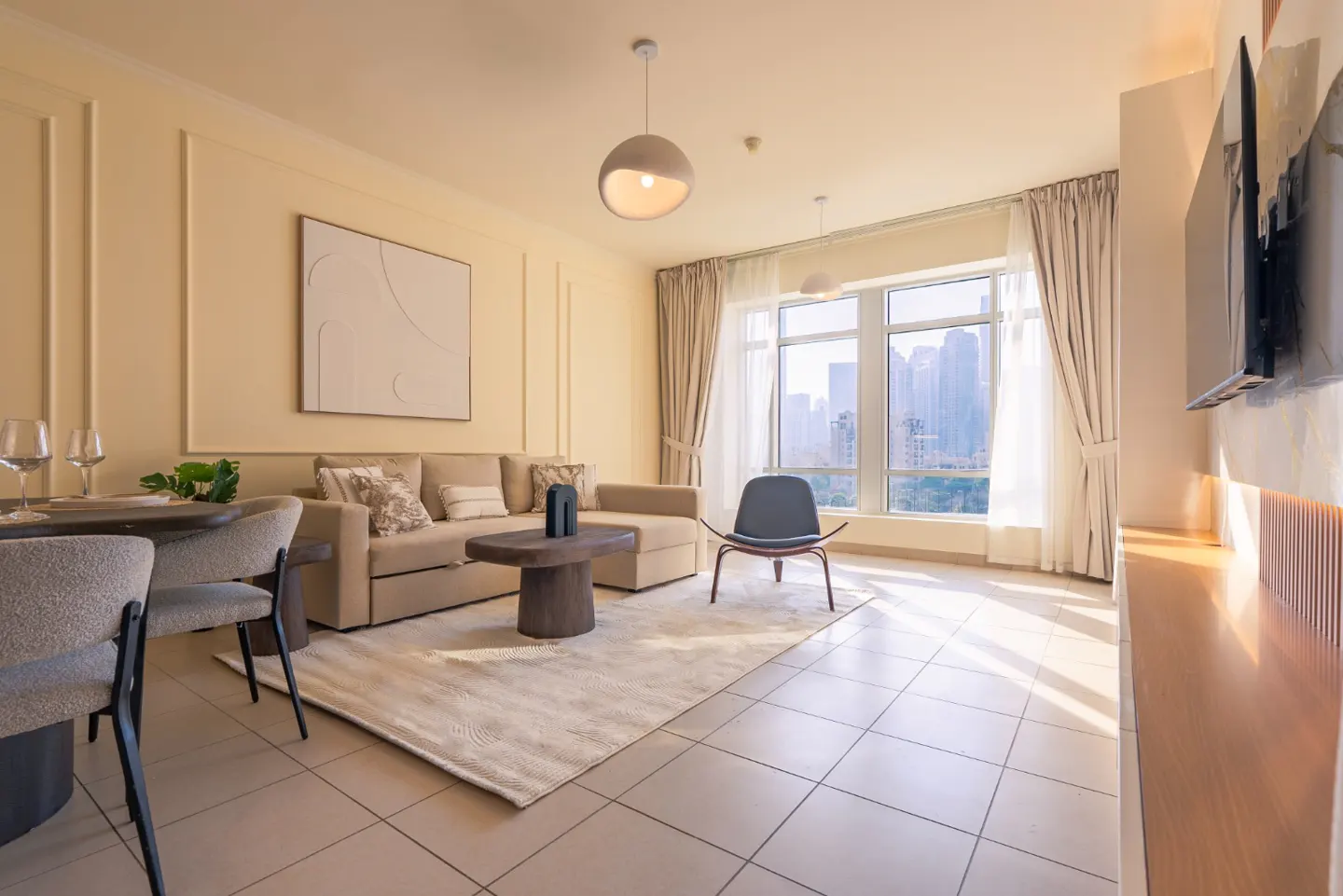 Living room with beige sofa, wood table, and city view through large windows. Neutral tones and modern decor.