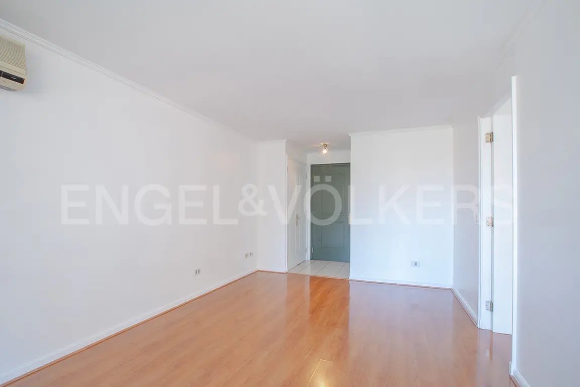 Bright, empty room with wood floors and white walls. A doorway is visible in the background. Engel & Völkers logo on the wall.