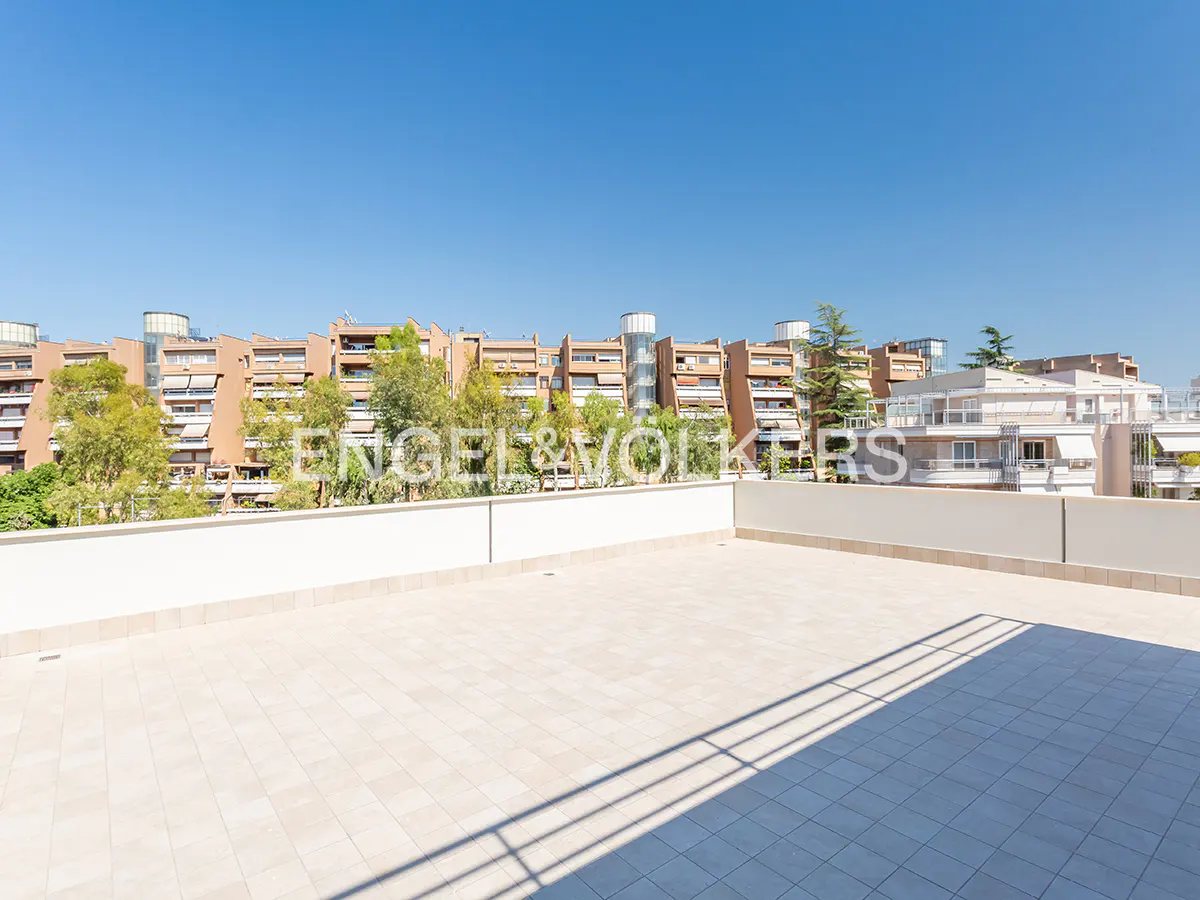 Spacious rooftop terrace with light-colored tiles, white railings, and a view of surrounding apartment buildings and trees.