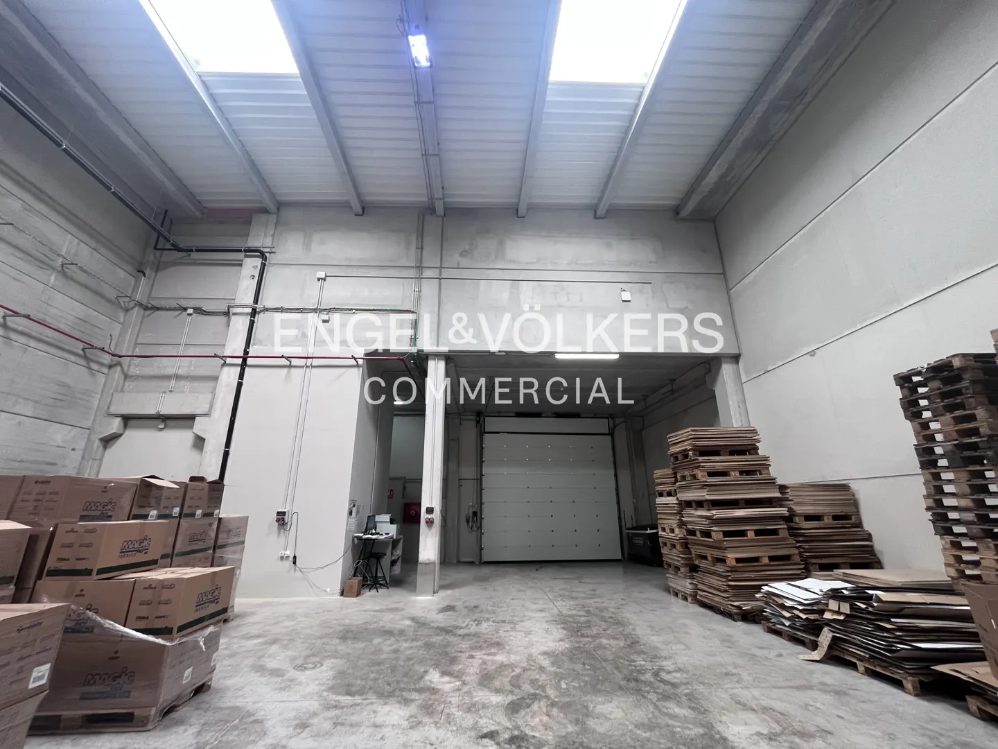 A warehouse interior with boxes, pallets, and an Engel & Völkers Commercial sign above a closed loading dock door.