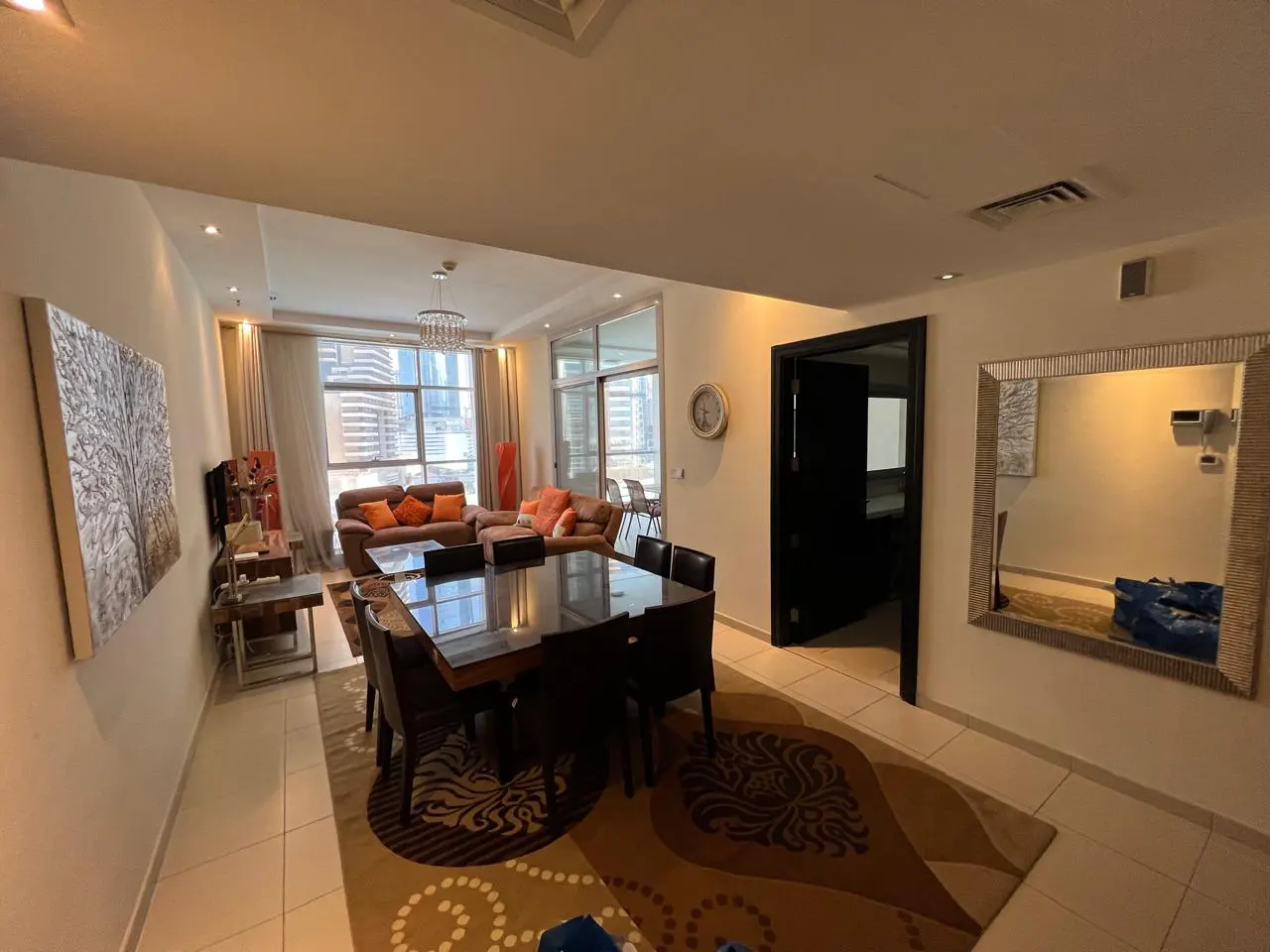 A wide shot of a living and dining area with a brown sofa, dining table, and a large mirror.