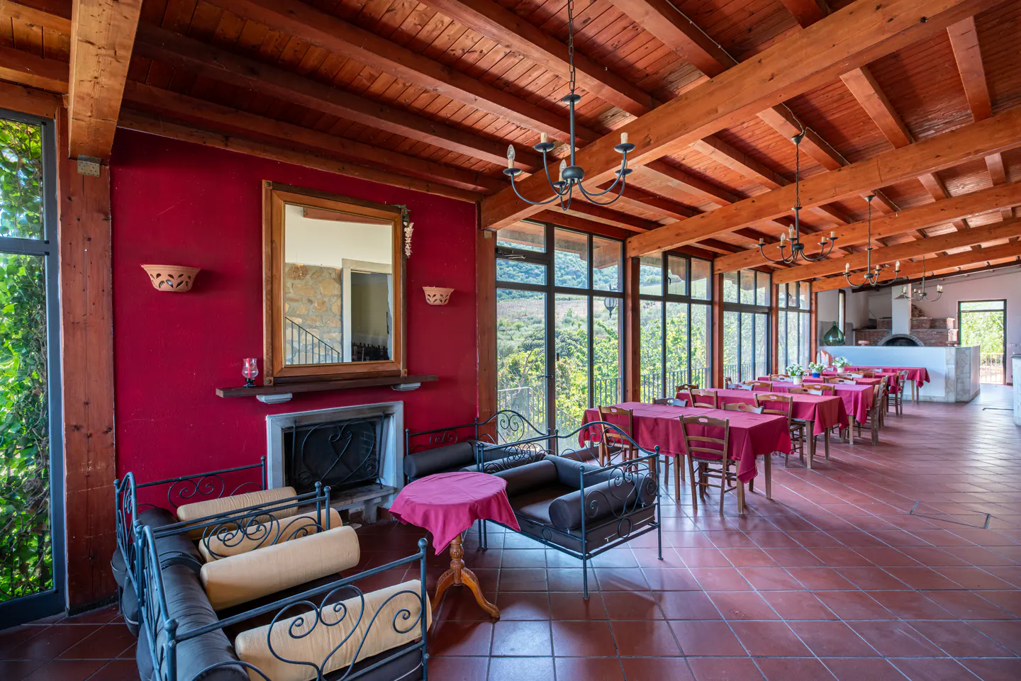 Interior of a restaurant with red walls, wooden ceiling, tables with red tablecloths, and large windows.