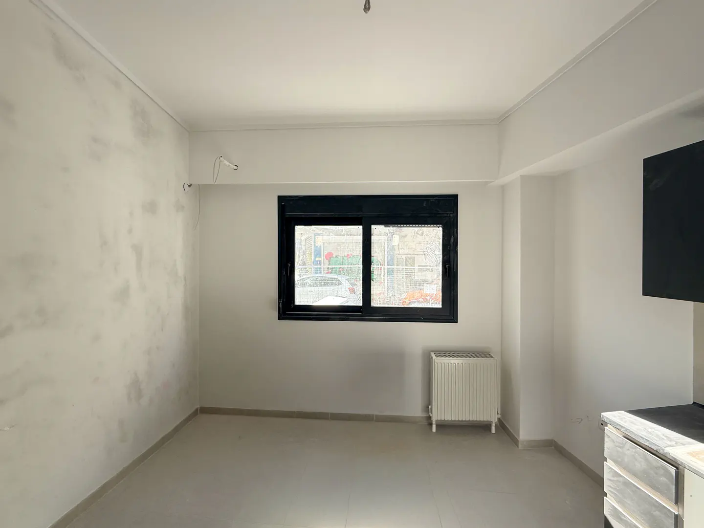 Bright, empty room with white walls, a black-framed window, and a radiator. The wall on the left has some discoloration.
