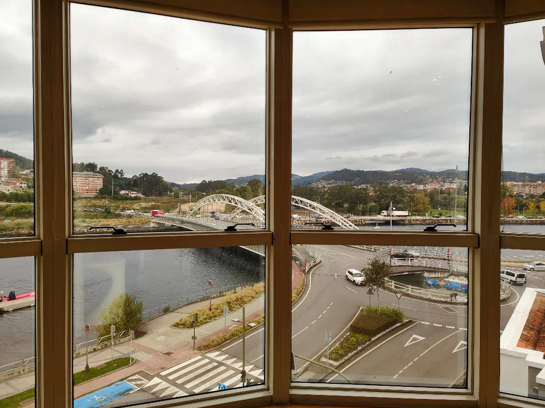 View from a window overlooking a river, bridge, and city streets on a cloudy day.