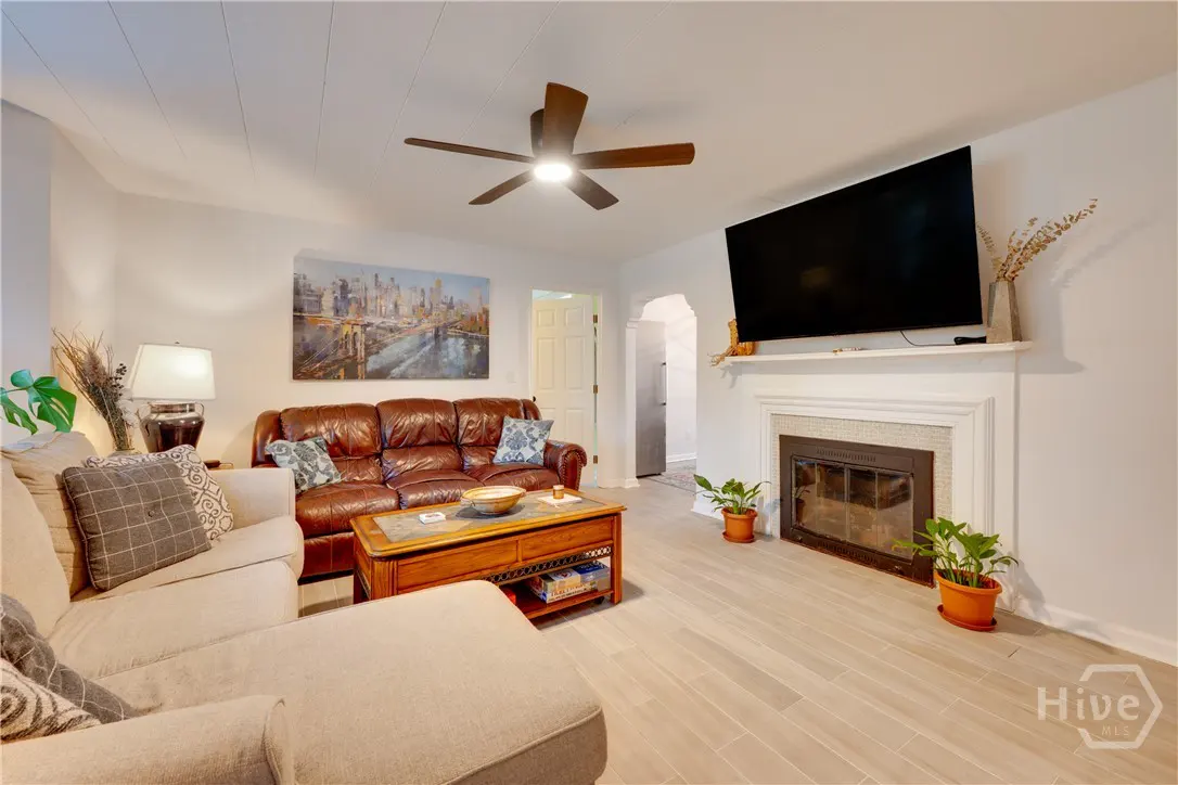 Living room with a beige sectional, brown leather sofa, wooden coffee table, fireplace with TV, and city skyline wall art.