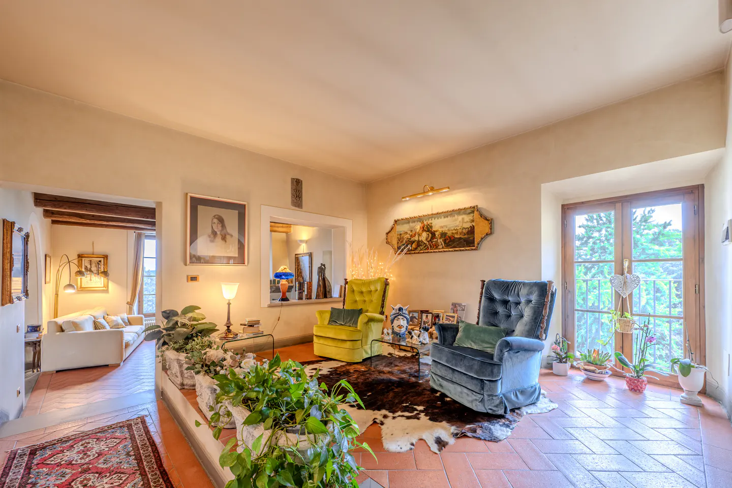 A living room with a blue armchair, a yellow armchair, and a cowhide rug on a terracotta tile floor.