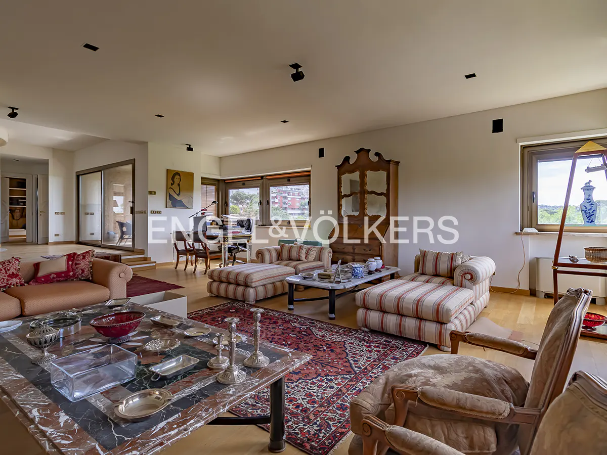 A spacious living room with sofas, a marble table, and a red patterned rug on a wooden floor.