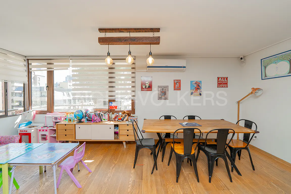 Bright room with wood floors, a long wood table with black chairs, and a children's play area with a toy kitchen and colorful table.