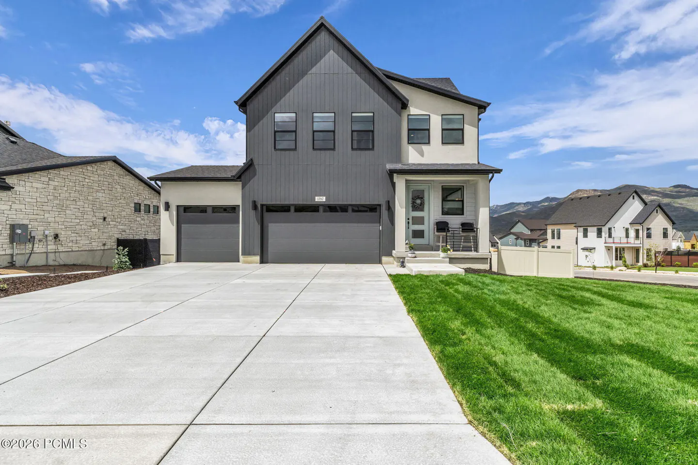 Two-story home with gray and white siding, a two-car garage, and a concrete driveway. Green lawn in front. Blue sky.
