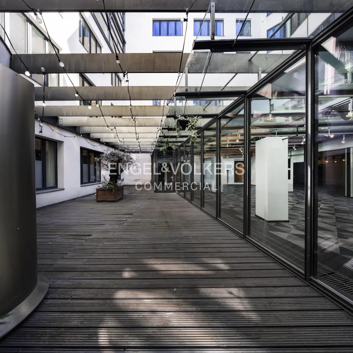 Outdoor commercial space with wood floors, glass walls, and string lights. Engel & Volkers logo visible.