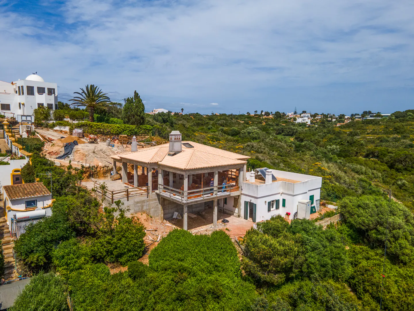 Aerial view of a house under construction with a tan roof, surrounded by green trees and a blue sky.