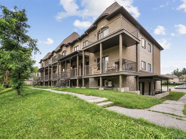 A tan brick townhouse with balconies and stairs, set on a green lawn under a blue sky.