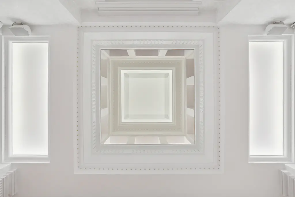 Looking up at a white ceiling with square recessed panels, windows, and speakers.
