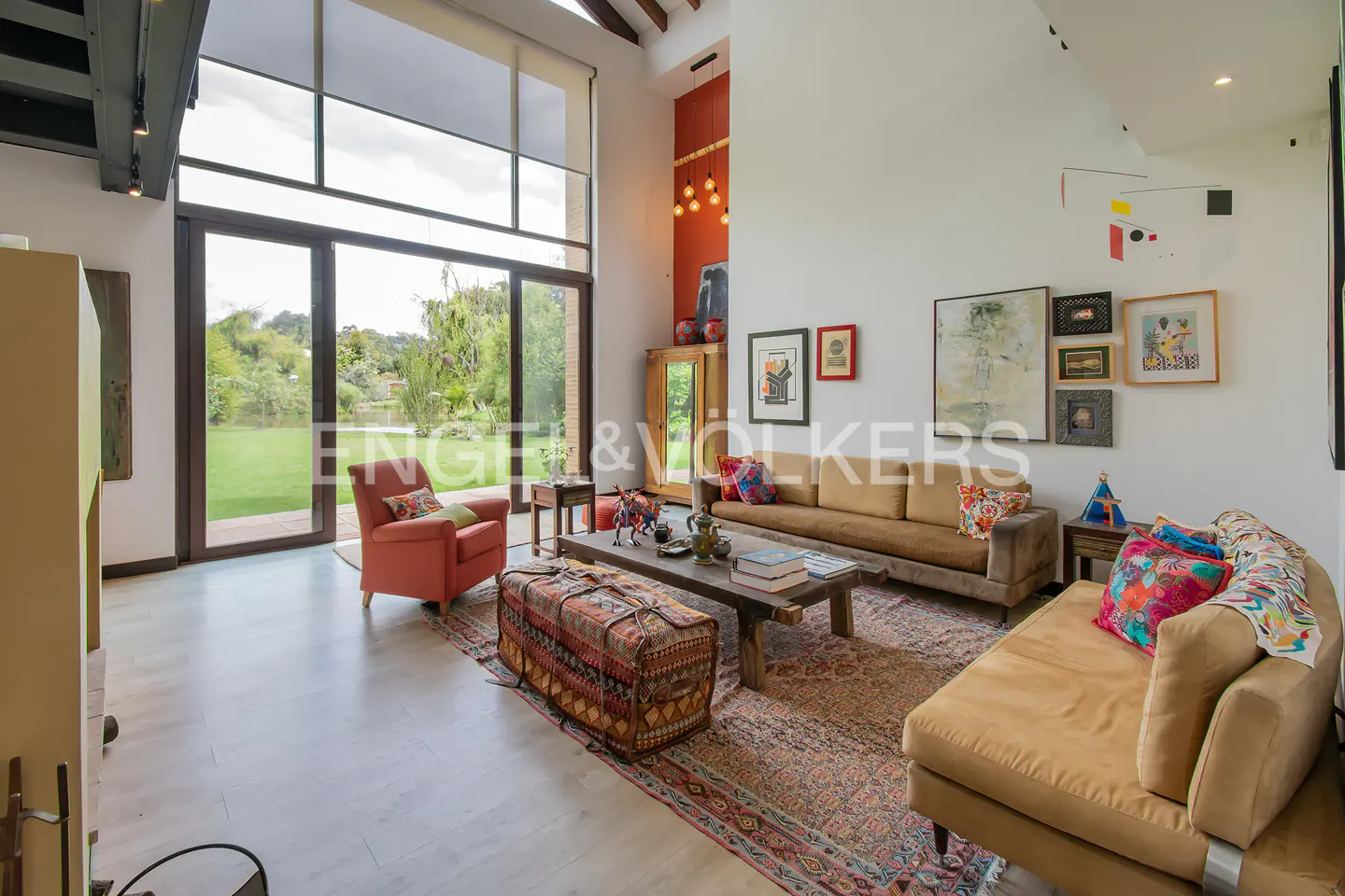A bright living room with a high ceiling, large windows, sofas, a rug, and artwork on the walls.